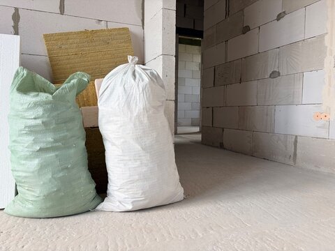 Construction waste is collected in large bags near the wall in an unfinished room