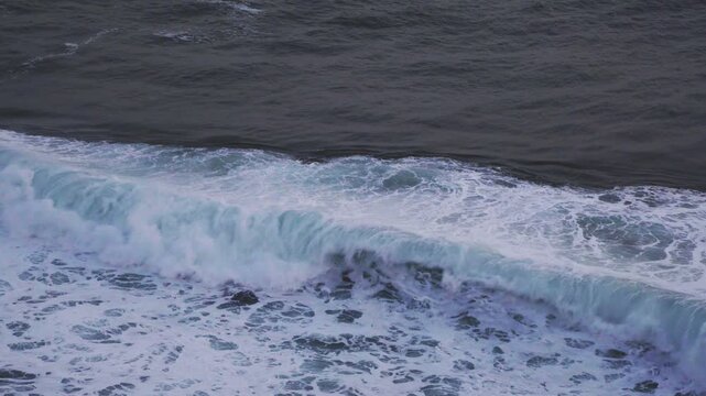 Large waves rolled in the middle of the sea, with white foam visible. Elevated view