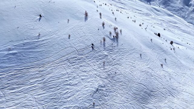 Aerial view of snow-covered mountain slope in Nauders with ski tracks and scattered trees under bright sunlight in Nauders, Tyrol, Austria.