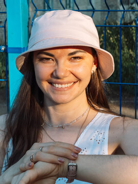 Portrait of smiling young woman in pink bucket hat sitting outdoors in summer sunlight.