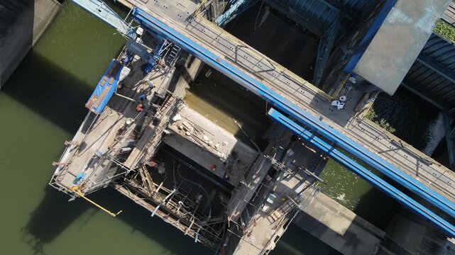 Aerial view of bridge construction site with scaffolding and blue steel structures over the river in Banyumas Regency, Central Java, Indonesia.