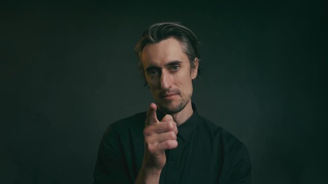 Adult man in black collared shirt pointing gestures in dark studio, soft moody lighting, authority and discretion concepts
