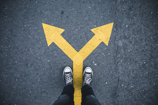 Person standing at a y shaped fork in the road with two directional arrows decision direction standing uncertainty motivation perspective movement conceptual lifestyle strategy