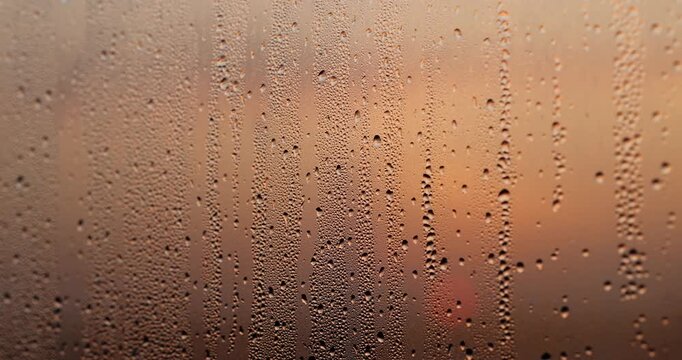 Drops of water on the transparent orange glass, the window glass is covered with small drops of clear water due to high humidity