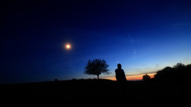 Silhouette of a person in nature observing night sky, Moon, stars and planets from a remote location.