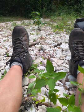 Punto di vista in prima persona di un escursionista in pausa, con gli scarponi appoggiati sui sassi di un letto di fiume