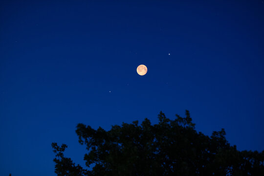 Full Moon on a twilight sky with landscape silhouettes.