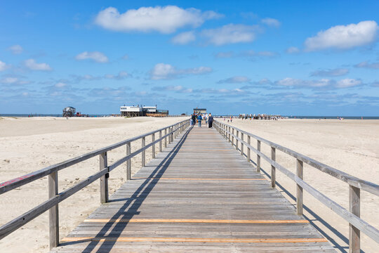 Beach of Sankt Peter-Ording with pile dwellings and hooded beach chairs on a summer day, view from the wooden sea bridge