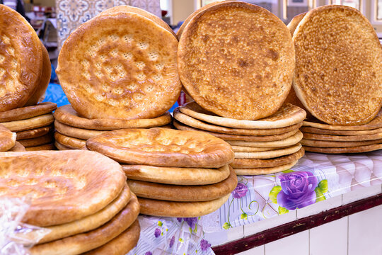 Traditional Uzbek flatbread stacked in piles at a bazaar counter in Bukhara. Golden round loaves with decorative patterns displayed for sale, ideal for food culture and travel content.