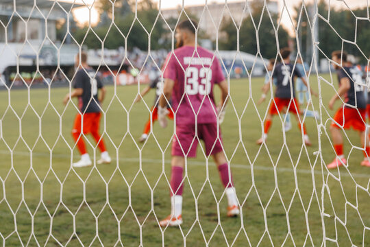 Dynamic soccer action seen through goal net, football ball hitting mesh during match in professional sports stadium competition concept
