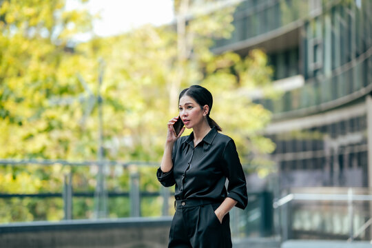 Businesswoman making business phone call outside office building. Professional discussing work, communicating with clients, managing tasks and using smartphone for remote business.