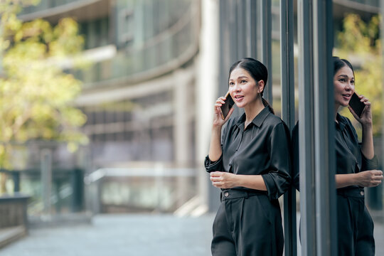 Businesswoman smiling during phone conversation beside modern office. Professional using smartphone for business networking, client communication and productive remote work.