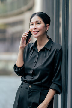 Businesswoman talking on smartphone while leaning against modern office building. Professional communicating with clients, building business relationships and working remotely with mobile technology.