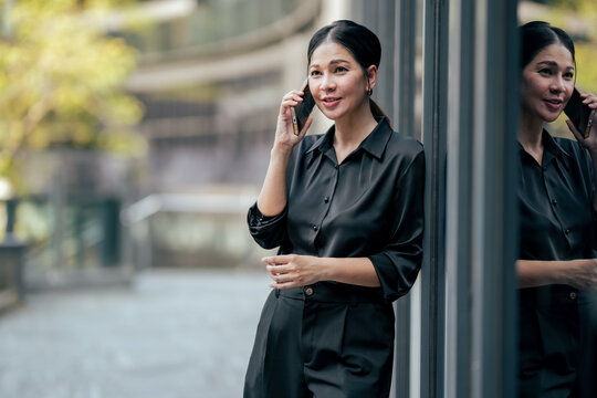 Businesswoman having pleasant phone conversation outside corporate office. Professional using smartphone for business communication, client support, networking and flexible remote work.