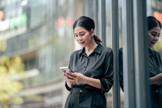 Businesswoman checking messages on smartphone outside office building. Professional using mobile technology for business communication, online collaboration, scheduling and digital productivity.
