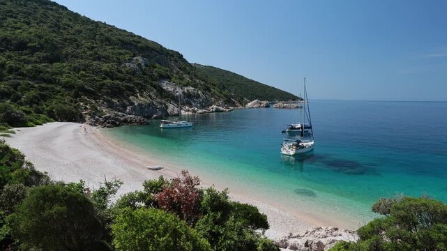 Sveti Ivan beach, pebble cove on Cres Island, Croatia, showing turquoise crystal clear Adriatic sea water, surrounded by green hills, with a sailboat anchored near coastline in Cres Island of Croatia