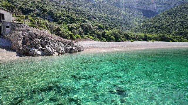 Sveti Ivan Beach on Cres Island, Croatia, showing clear turquoise Adriatic Sea water lapping pebble beach with small boat anchored in the tranquil bay under bright summer sky in Cres Island of Croatia