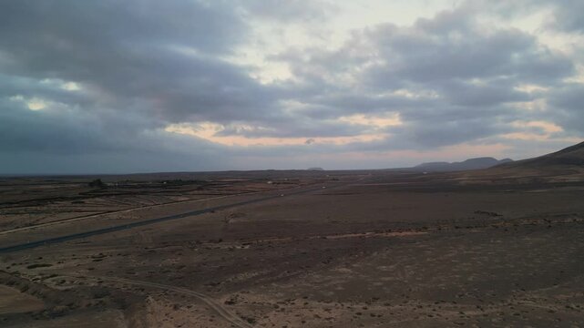 Aerial view of the arid desert landscape with a road stretching through the volcanic terrain under a cloudy sky in El Cotillo, Canary Islands, Spain.
