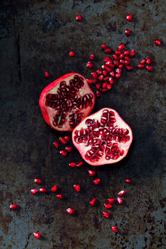 Two halves of pomegranate and pomegranate seed on dark metal
