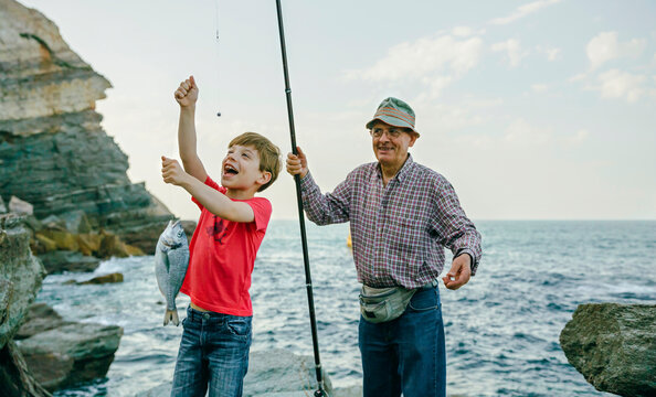 Happy boy holding fish on fishing line caught by his grandfather