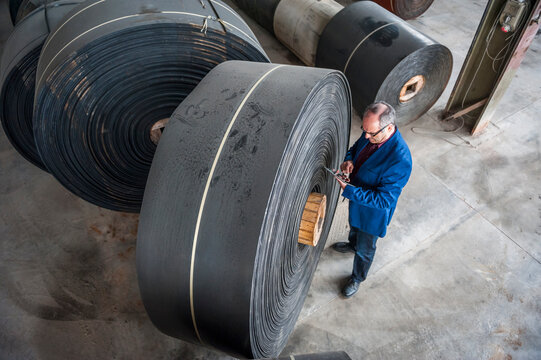Manager with digital tablet in factory hall with rolls of rubber