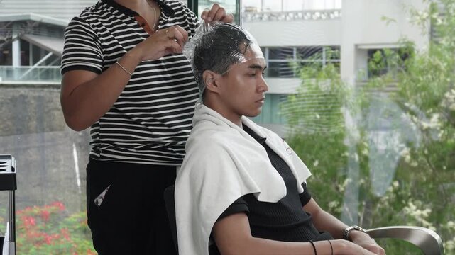 Hair wrapped in plastic wrap during professional cellophane hair treatment after rebonding for Southeast Asian man in his early 20s