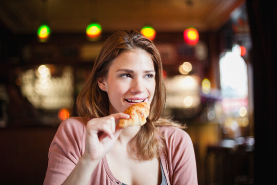 France, Paris, portrait of happy young woman eating a croissant in a cafe