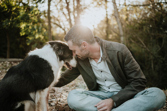 A man is petting his border collie dog outdoors at sunset