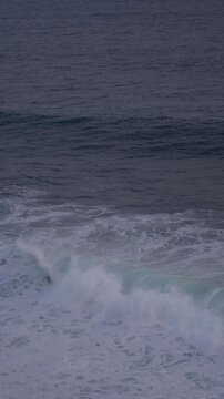 Large waves rolled in the middle of the sea, with white foam visible. Elevated view