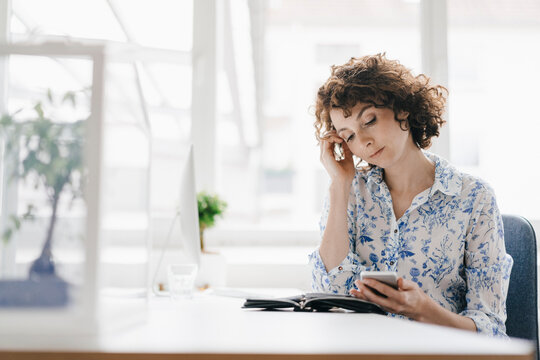 Businesswoman in office with smartphone and diary, looking worried