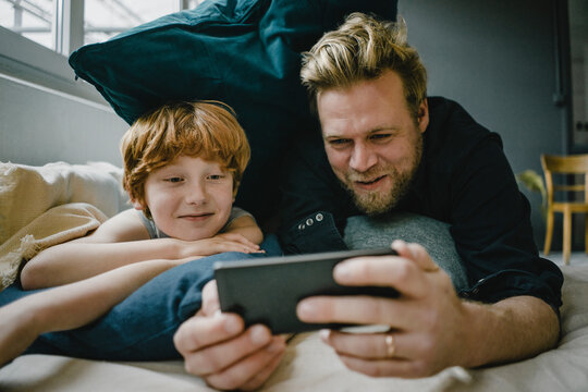 Portrait of father and son lying on couch looking at cell phone
