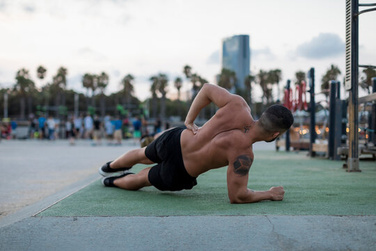 Barechested muscular man doing side planks outdoors