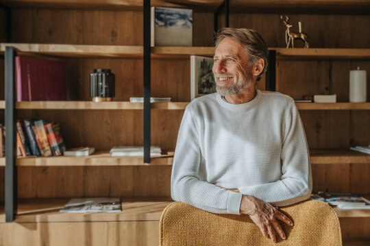 Smiling mature man looking away while standing at chair at home