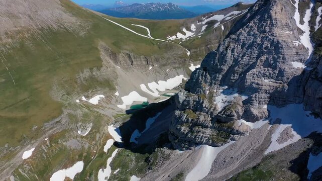 Aerial view of the glacial Lago di Pilato nestled between the rugged, snow-dusted peaks of the Sibillini Mountains in Montemonaco, Marche, Italy.