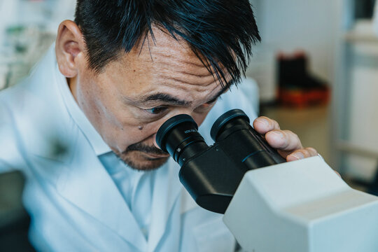 Male scientist looking though microscope while man standing in background at laboratory
