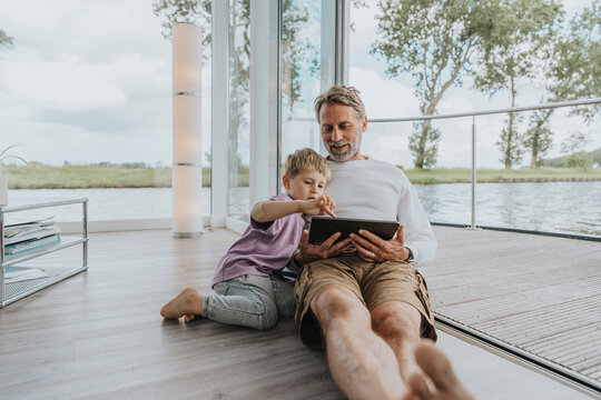 Smiling father with son using tablet PC sitting on floor
