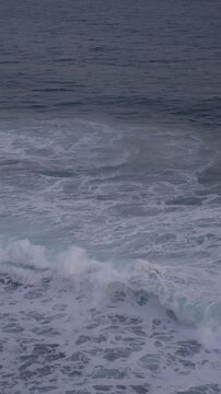 Large waves rolled in the middle of the sea, with white foam visible. Elevated view