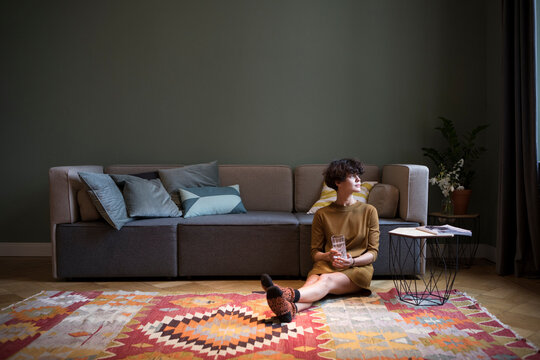 Young woman sitting on the floor in her living room looking through window