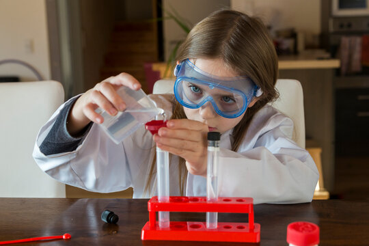 Girl wearing work coat and safety glasses using chemistry set at home