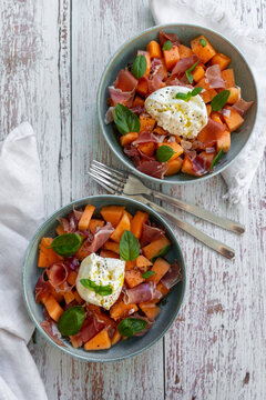 Cantaloupe salad with burrata and serrano ham on a rustic table
