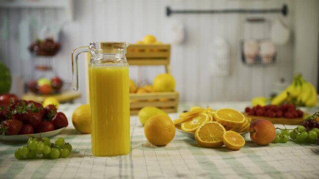 Orange's and pitcher of juice on kitchen counter near other fruit - medium, tracking shot