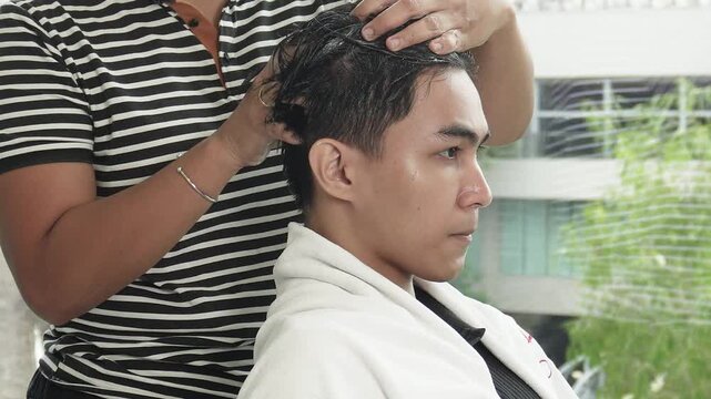 Hair stylist applying protein color cream before professional cellophane hair treatment for Southeast Asian man in his early 20s