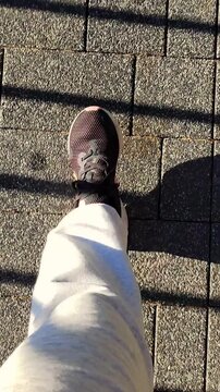 A foot in a dark sneaker moves across a tiled sidewalk under strong morning light and graphic shadows. The scene connects walking, mental focus, commuting habits, and simple urban wellbeing.