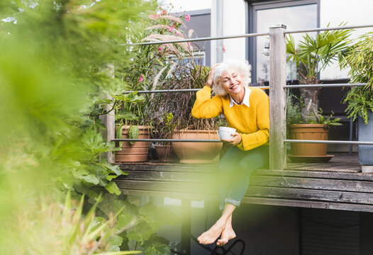 Mature woman with hand in hair sitting at home against railing