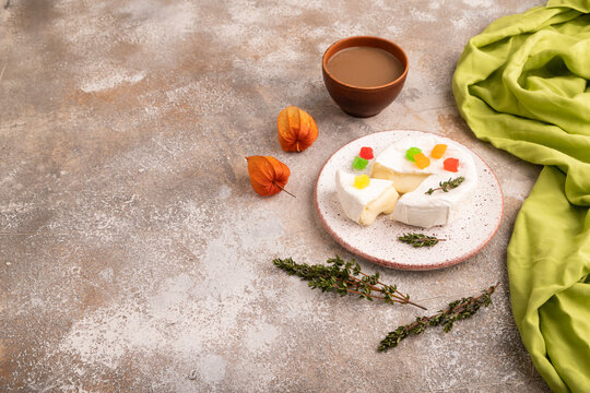 White Camembert mold cheese on brown concrete background and green textile, cup of coffee, side view, copy space