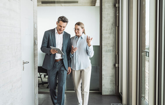 Smiling mature businessman discussing with businesswoman over tablet PC in office