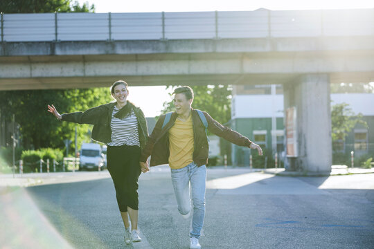A young man and woman run happily along a city street