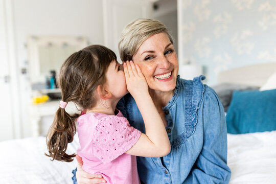 Girl whispering in mother's ear at home