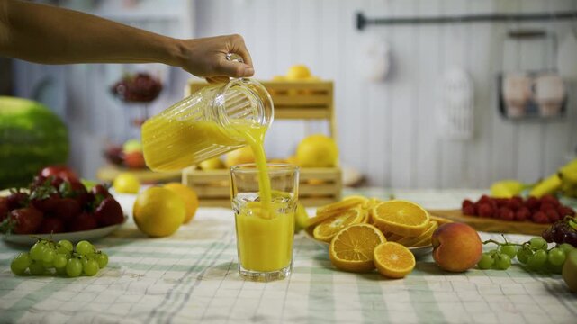 Hand pouring pitcher of orange juice into glass on kitchen counter, tracking shot