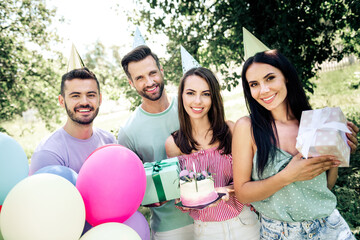 Obraz premium Friends celebrating a birthday party outdoors with cake, balloons and gifts, smiling young adults wearing party hats in a sunny garden